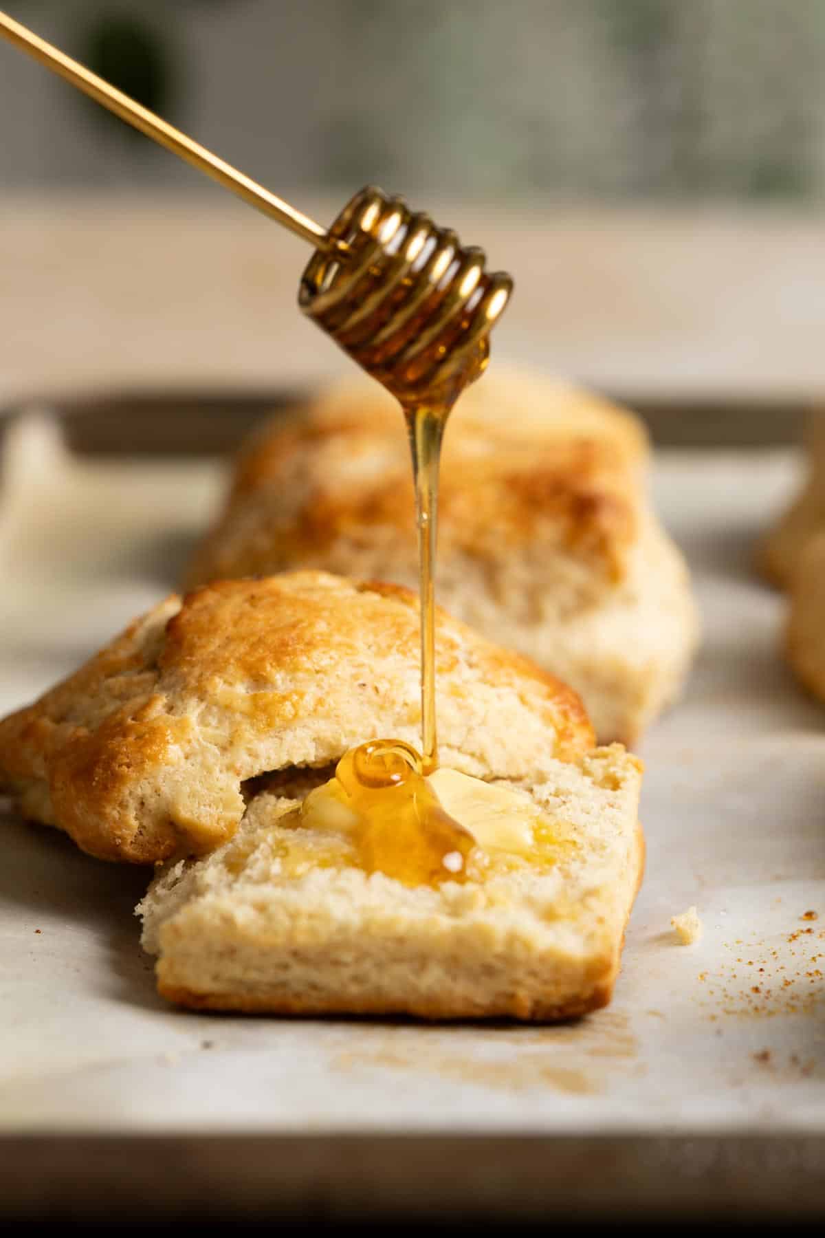 Honey is drizzling on a half sourdough biscuit.