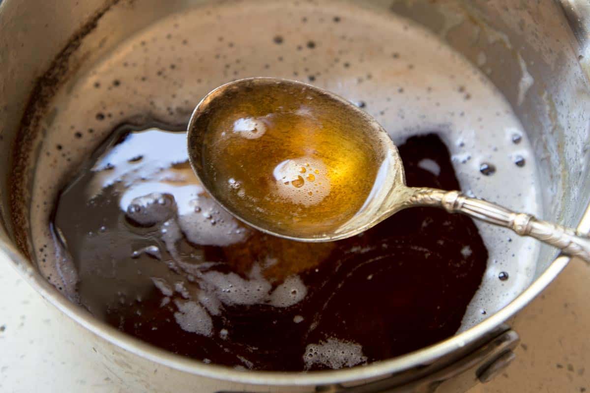 A spoon with brown butter hovering over a saucepan.