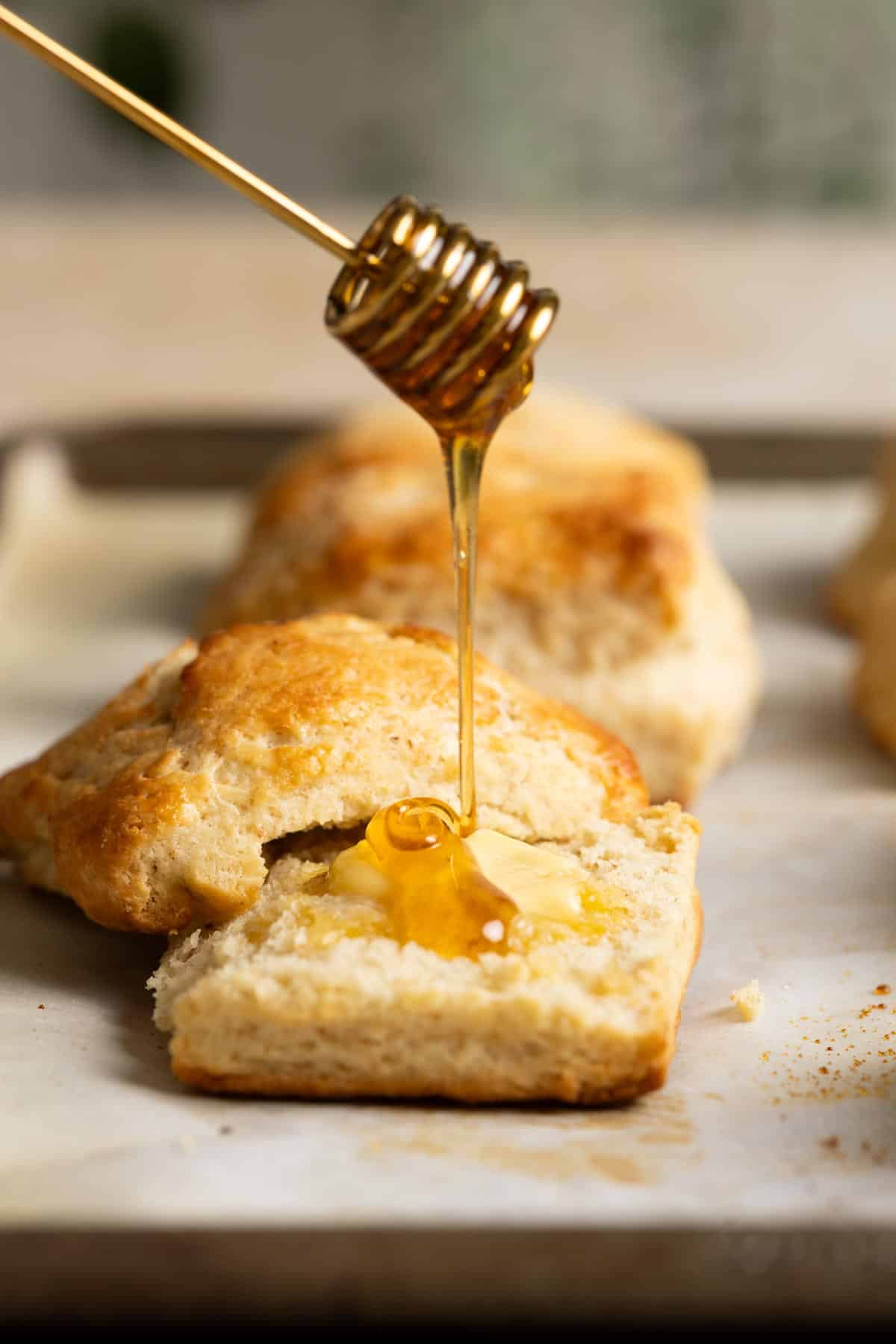 Honey drizzling on a sourdough biscuit sitting on a baking sheet.