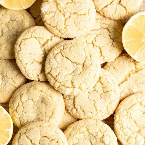 Sourdough lemon cookies piled on top of each other next to some halved lemons.