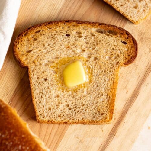 A slice of toasted whole wheat sourdough milk bread with a pat of butter on it.