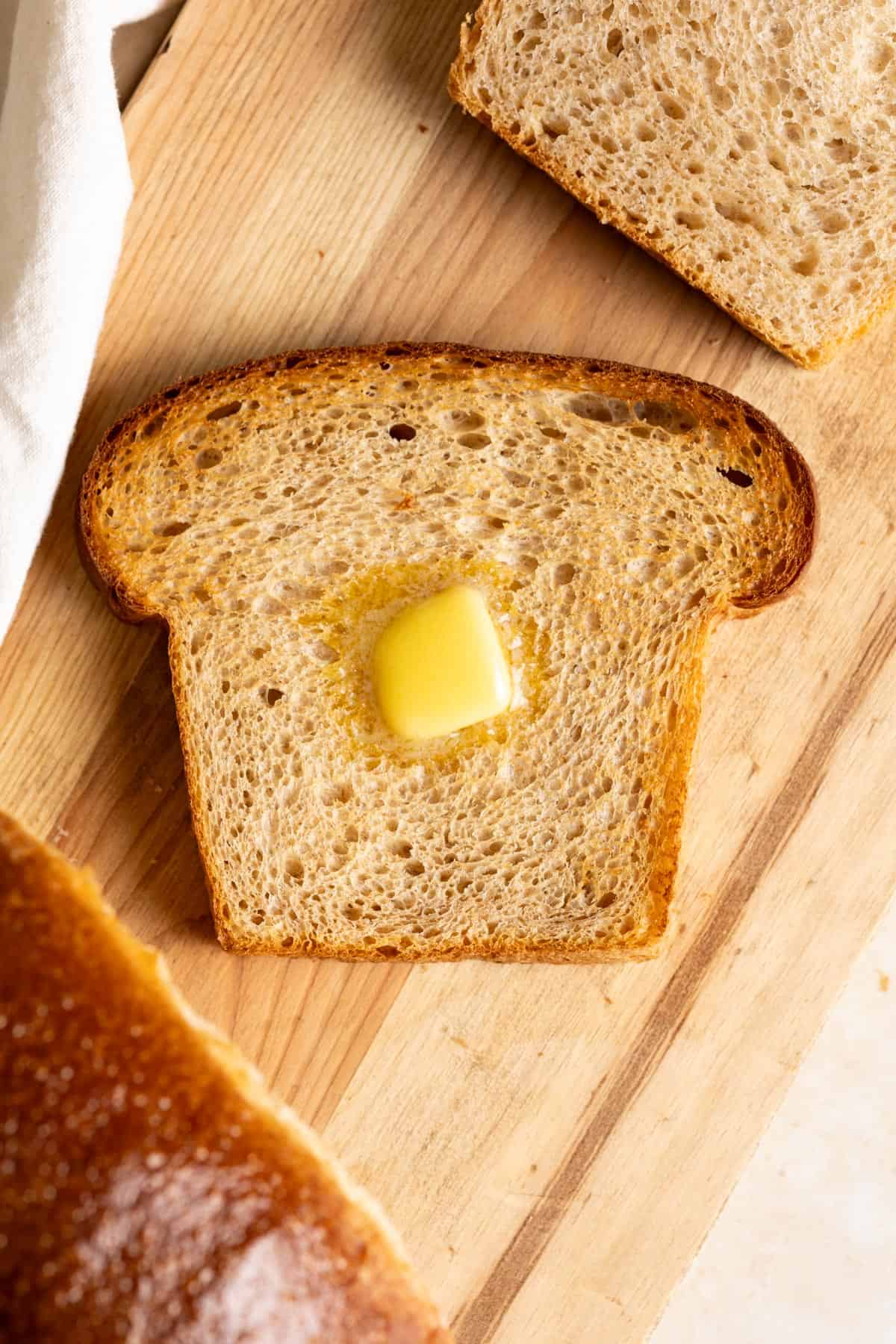 A slice of toasted whole wheat sourdough milk bread with a pat of butter on it.