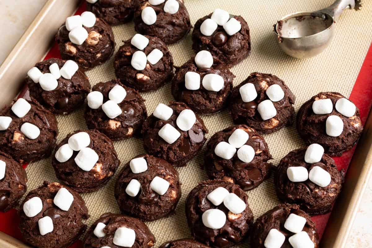 Chocolate cookie dough balls on a baking sheet with marshmallows on top.