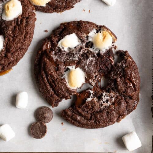 A sourdough chocolate cookie on a baking sheet being pulled apart, gooey marshmallows are in the middle.