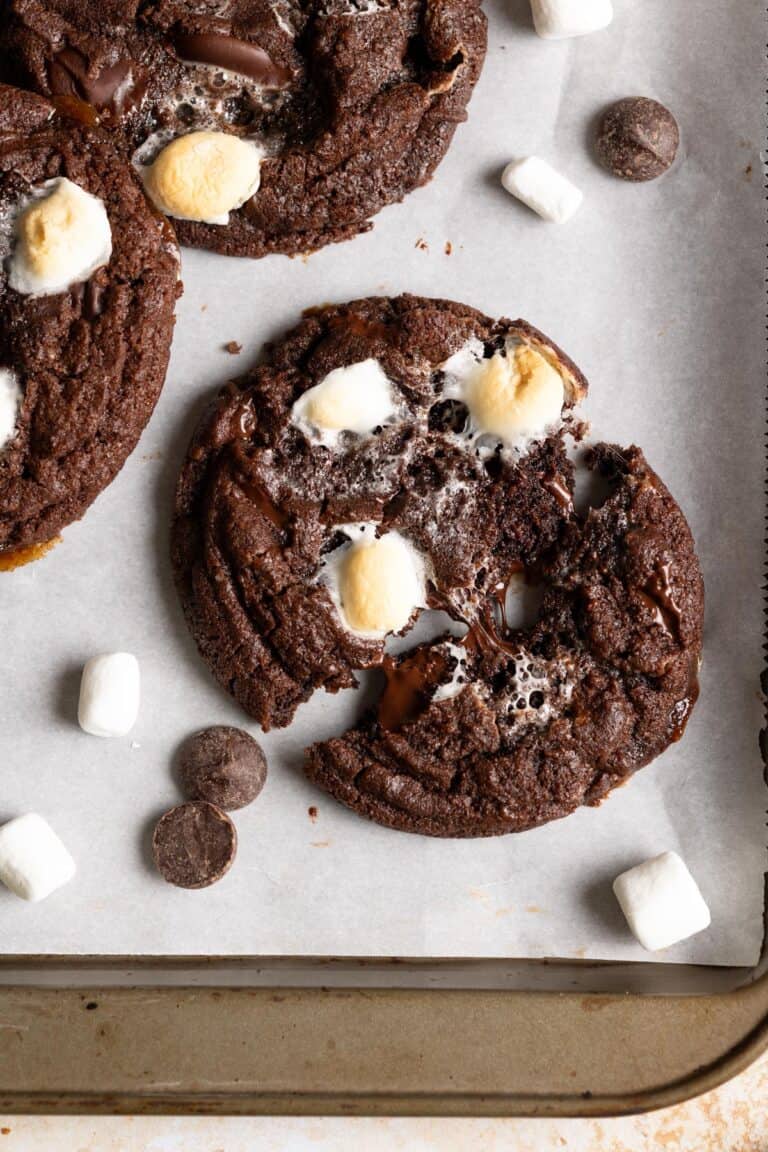 A sourdough chocolate cookie on a baking sheet being pulled apart, gooey marshmallows are in the middle.
