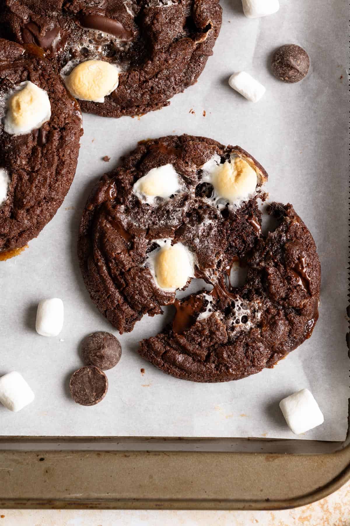 A sourdough chocolate cookie on a baking sheet being pulled apart, gooey marshmallows are in the middle.