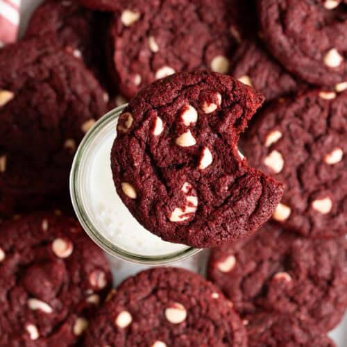 A sourdough red velvet cookie with a bite taken out of it sitting on a glass of milk.