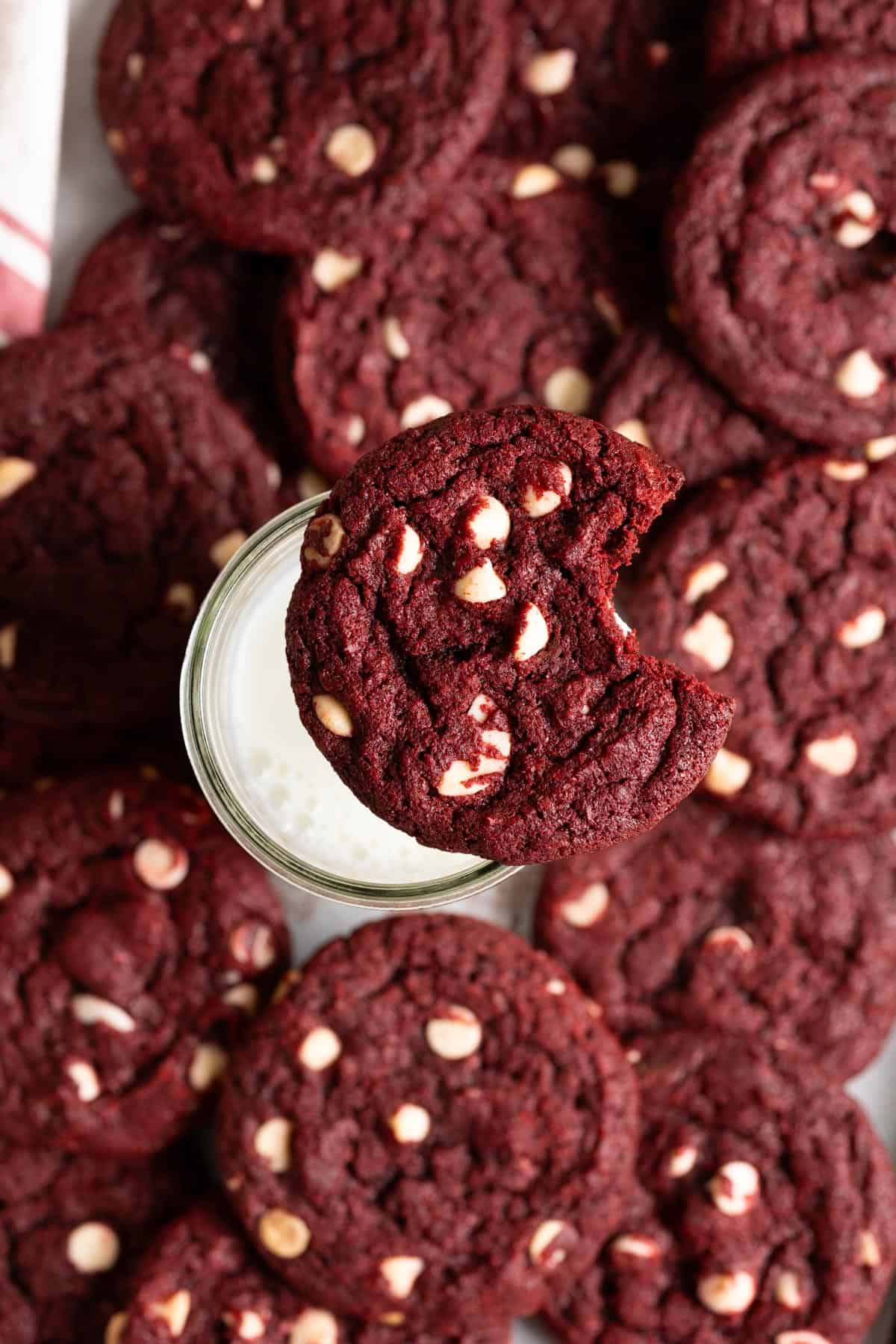 A sourdough red velvet cookie with a bite taken out of it sitting on a glass of milk.