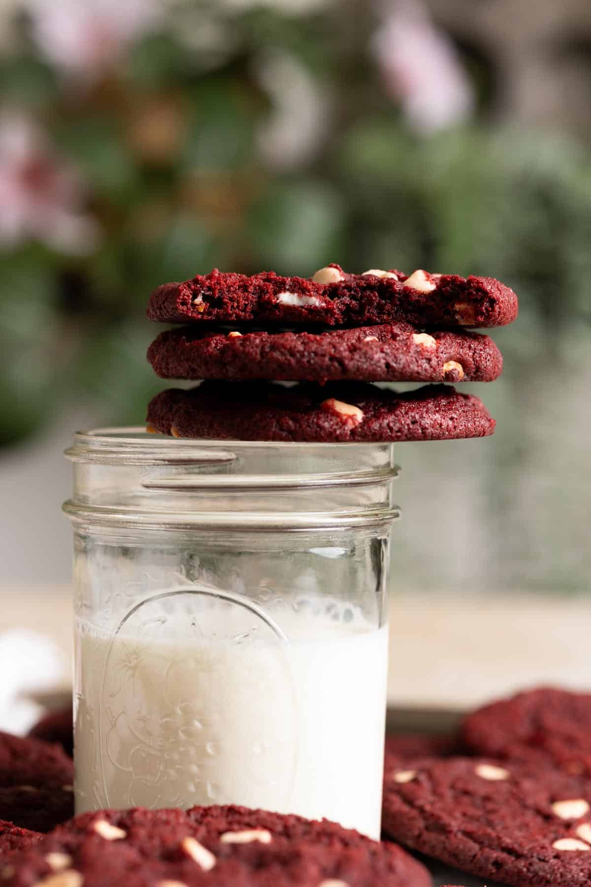 A stack of sourdough red velvet cookies resting on the edge of a glass of milk.