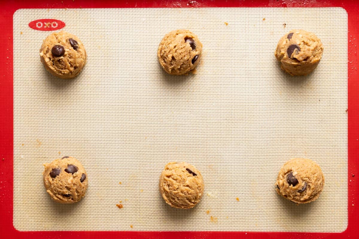6 sourdough chocolate chip cookies with toffee dough balls on a baking sheet.