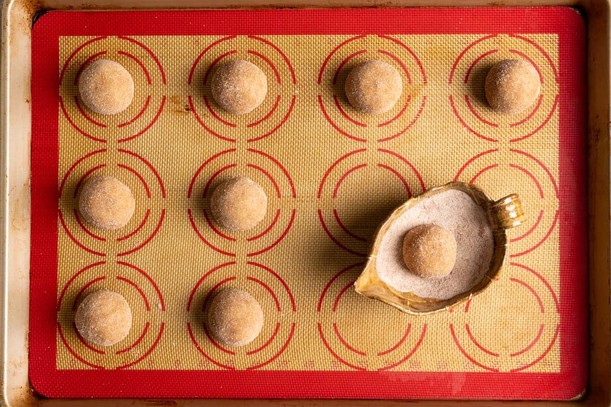 Sourdough snickerdoodle dough balls rolled in cinnamon sugar on a baking sheet.