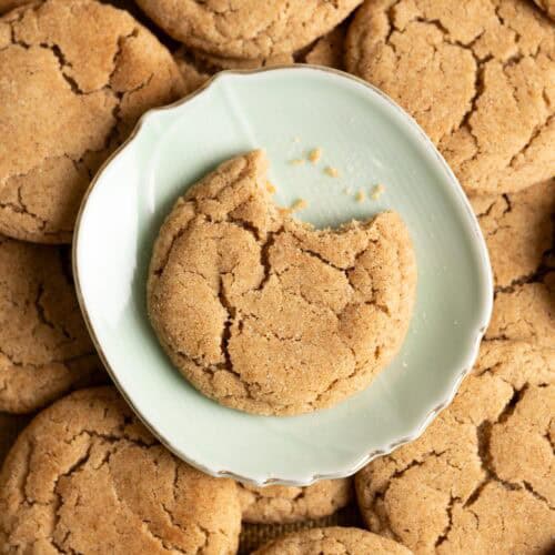 A bitten sourdough snickerdoodle cookie on a plate on top of a pile of cookies.