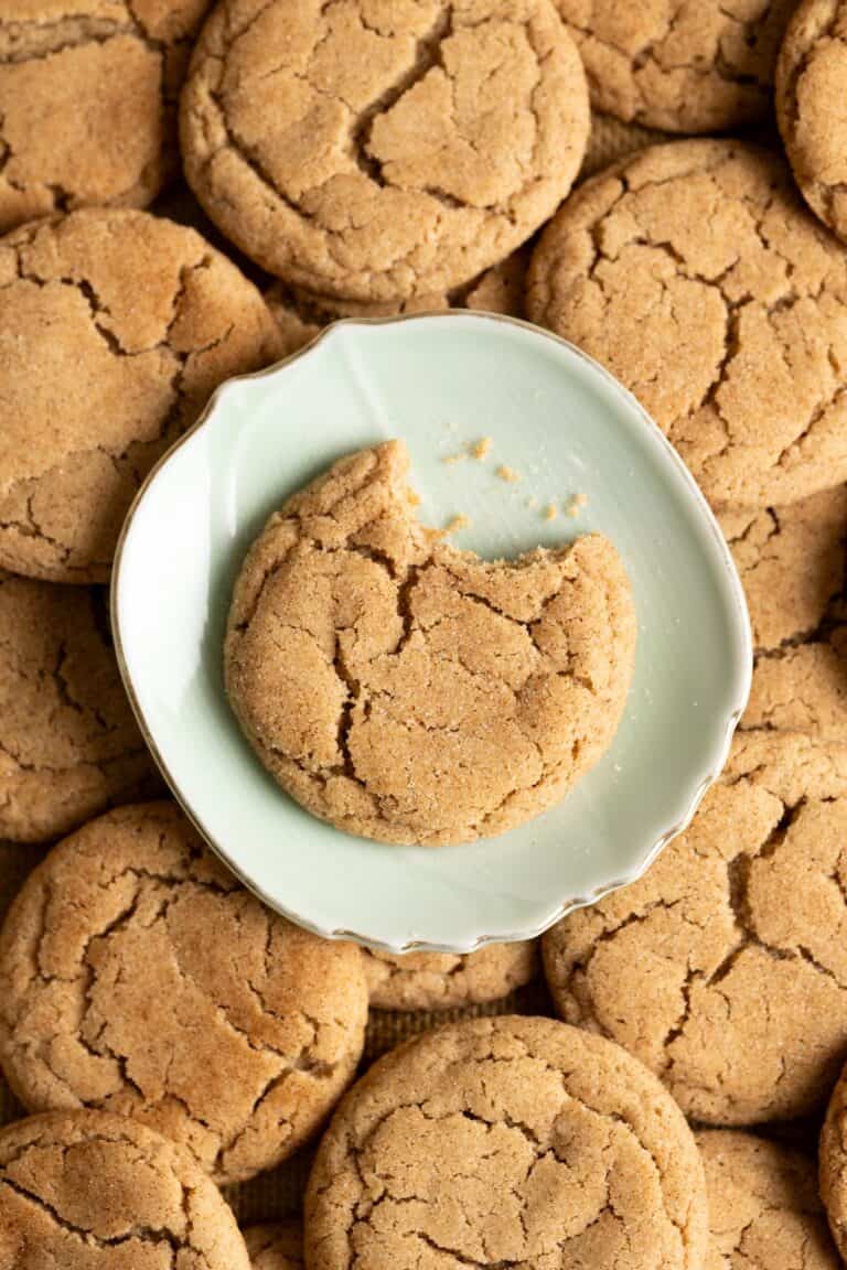A bitten sourdough snickerdoodle cookie on a plate on top of a pile of cookies.