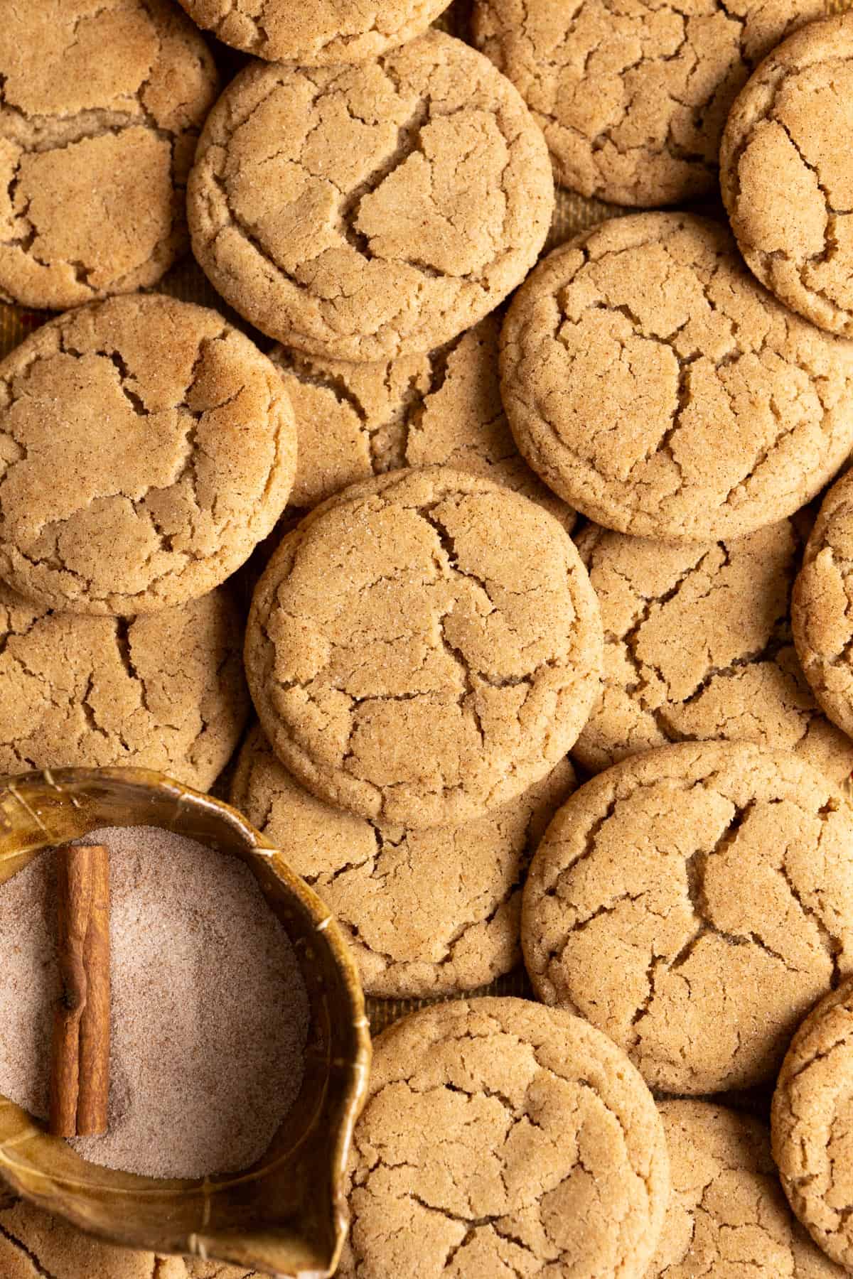 A pile of sourdough snickerdoodles next to a bowl of cinnamon sugar.