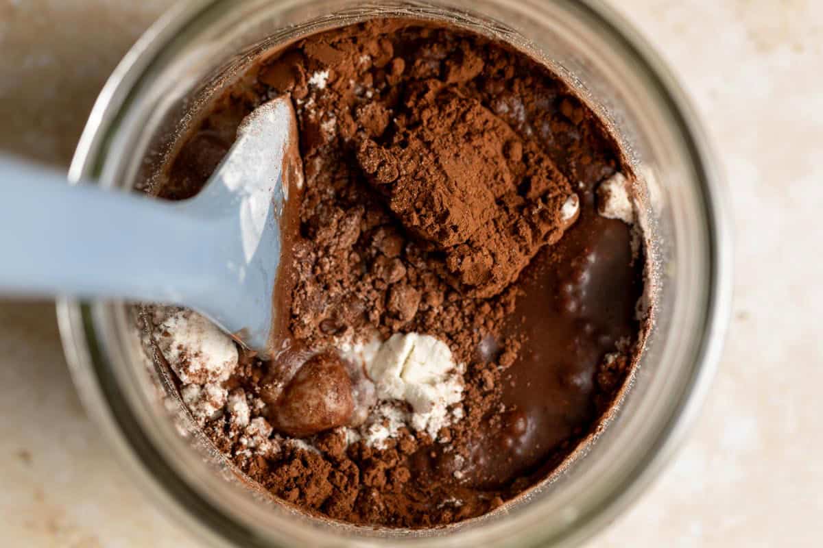 Top down view of cocoa powder, flour, and water in a jar with a spatula.