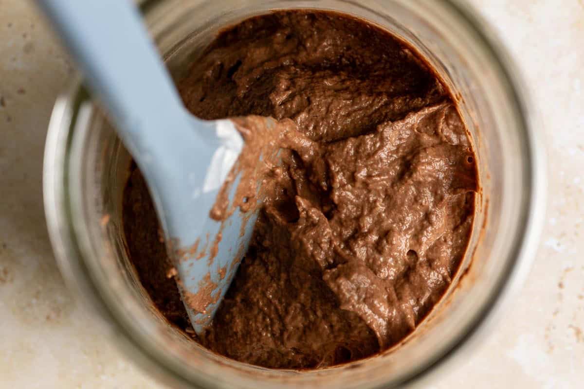 Top down view of chocolate starter ingredients mixed into a paste in a jar with a spatula.