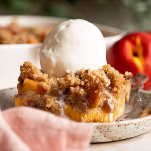 A slice of peach cobbler bread pudding on a plate with a scoop of vanilla ice cream on top.