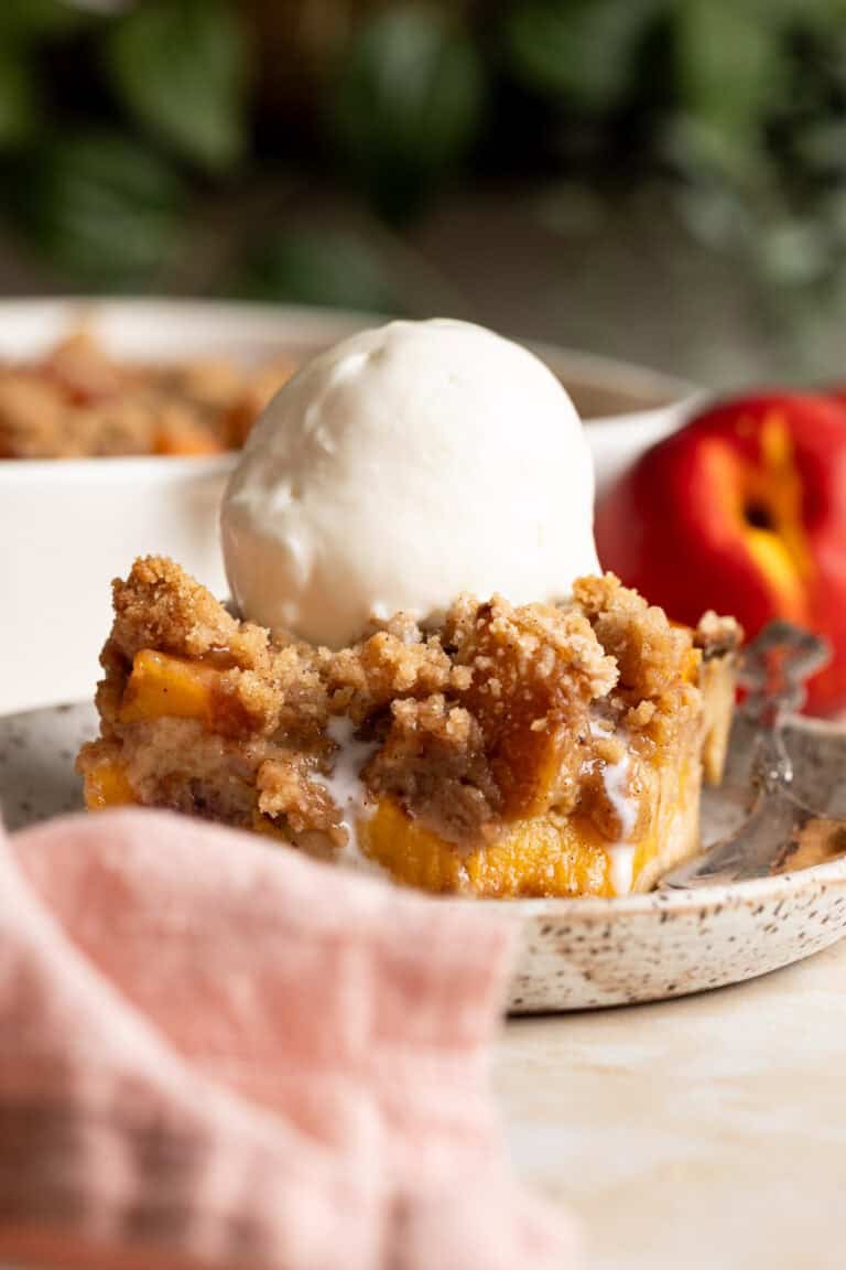 A slice of peach cobbler bread pudding on a plate with a scoop of vanilla ice cream on top.