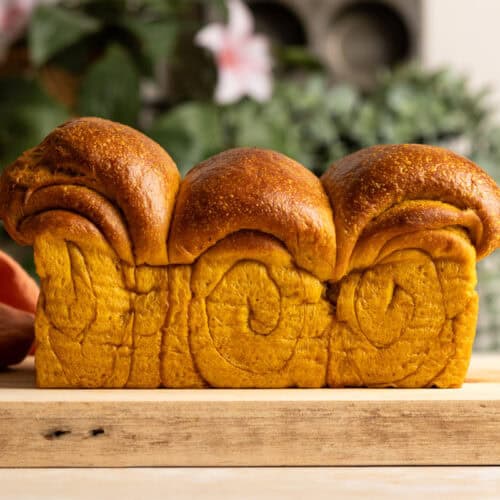A loaf of sourdough pumpkin milk bread on a wooden board.