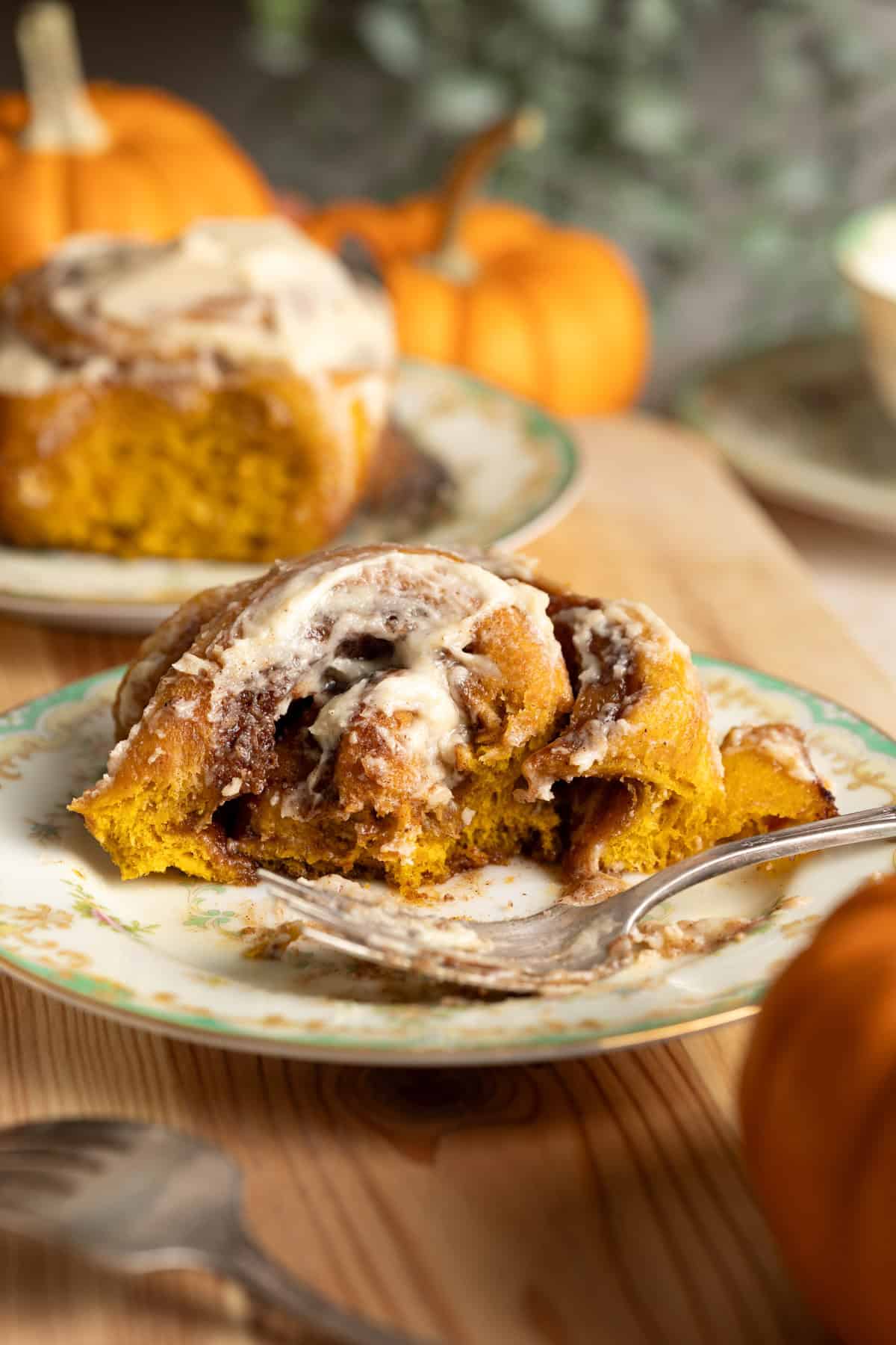 A half eaten pumpkin cinnamon roll on a plate.