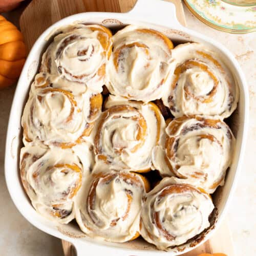 Frosted sourdough pumpkin cinnamon rolls in a square baking pan.