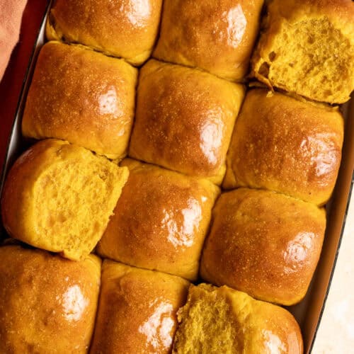 A tray of sourdough pumpkin dinner rolls with some rolls showing the soft interior.