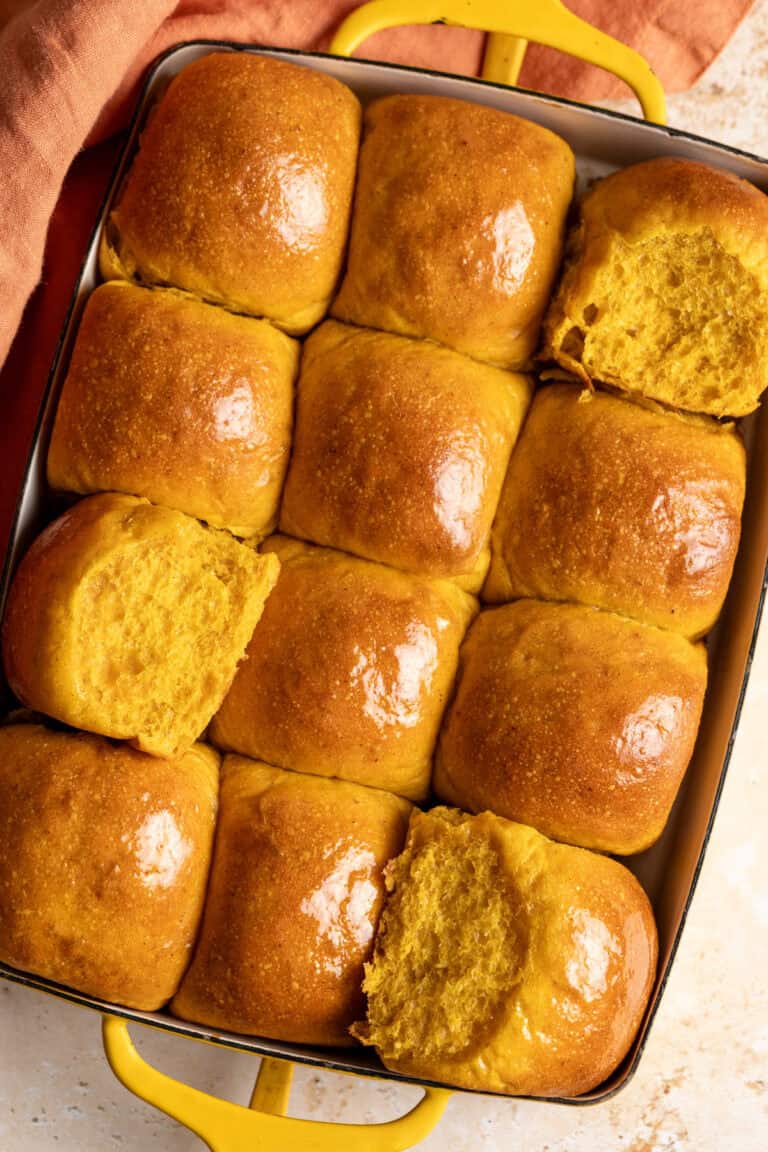 A tray of sourdough pumpkin dinner rolls with some rolls showing the soft interior.