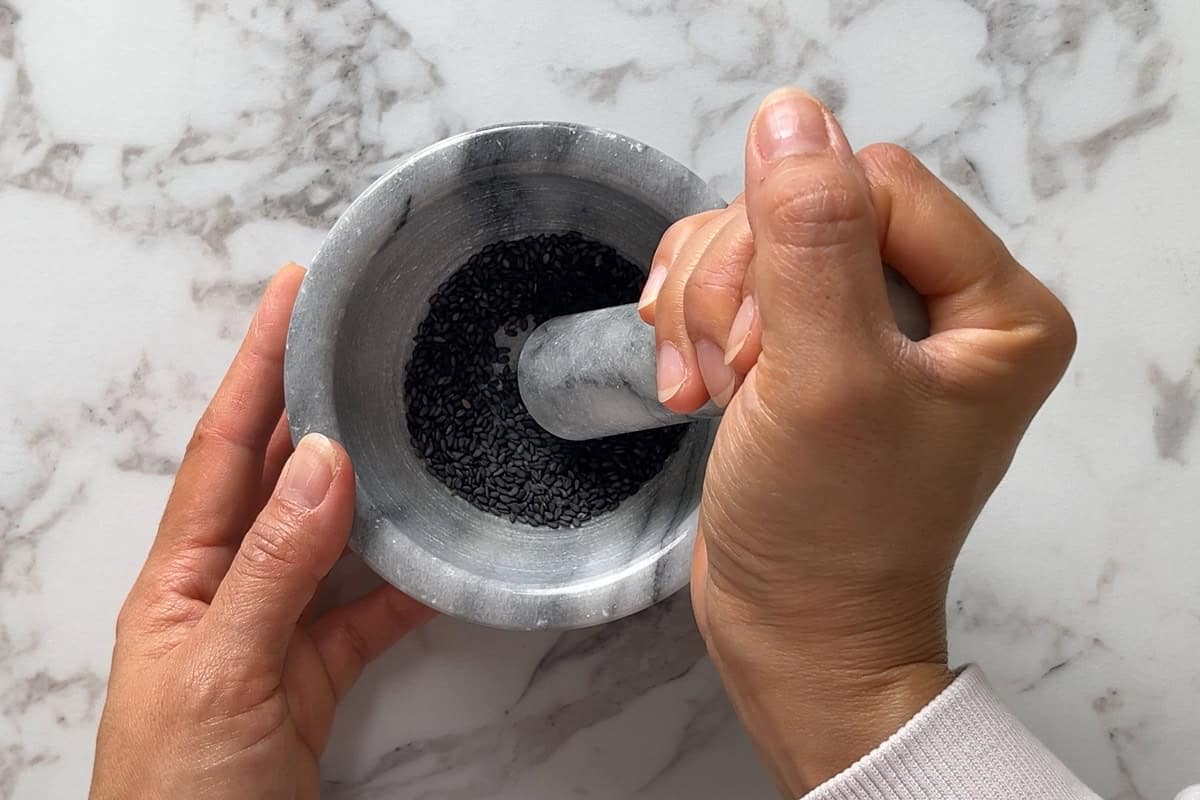 Grinding black sesame seeds using a pestle and mortar.